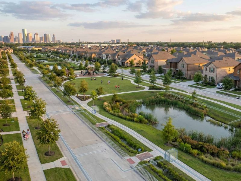 Lush suburban neighborhood with parks, ponds, and city skyline in the distance.
